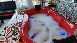 A red hot tub with bubbles, a black sofa, and a patterned floor. - Hotel Platinium Palace (Cusco)