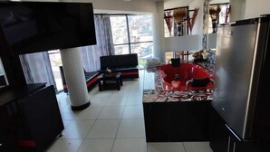 A modern living room with a black sofa, a coffee table, and a TV. There is a red bathtub in the corner and a refrigerator. - Hotel Platinium Palace (Cusco)