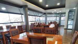 A spacious dining area with wooden tables and chairs, large windows offering views of the city, and a modern ceiling with recessed lighting. - Hotel Platinium Palace (Cusco)