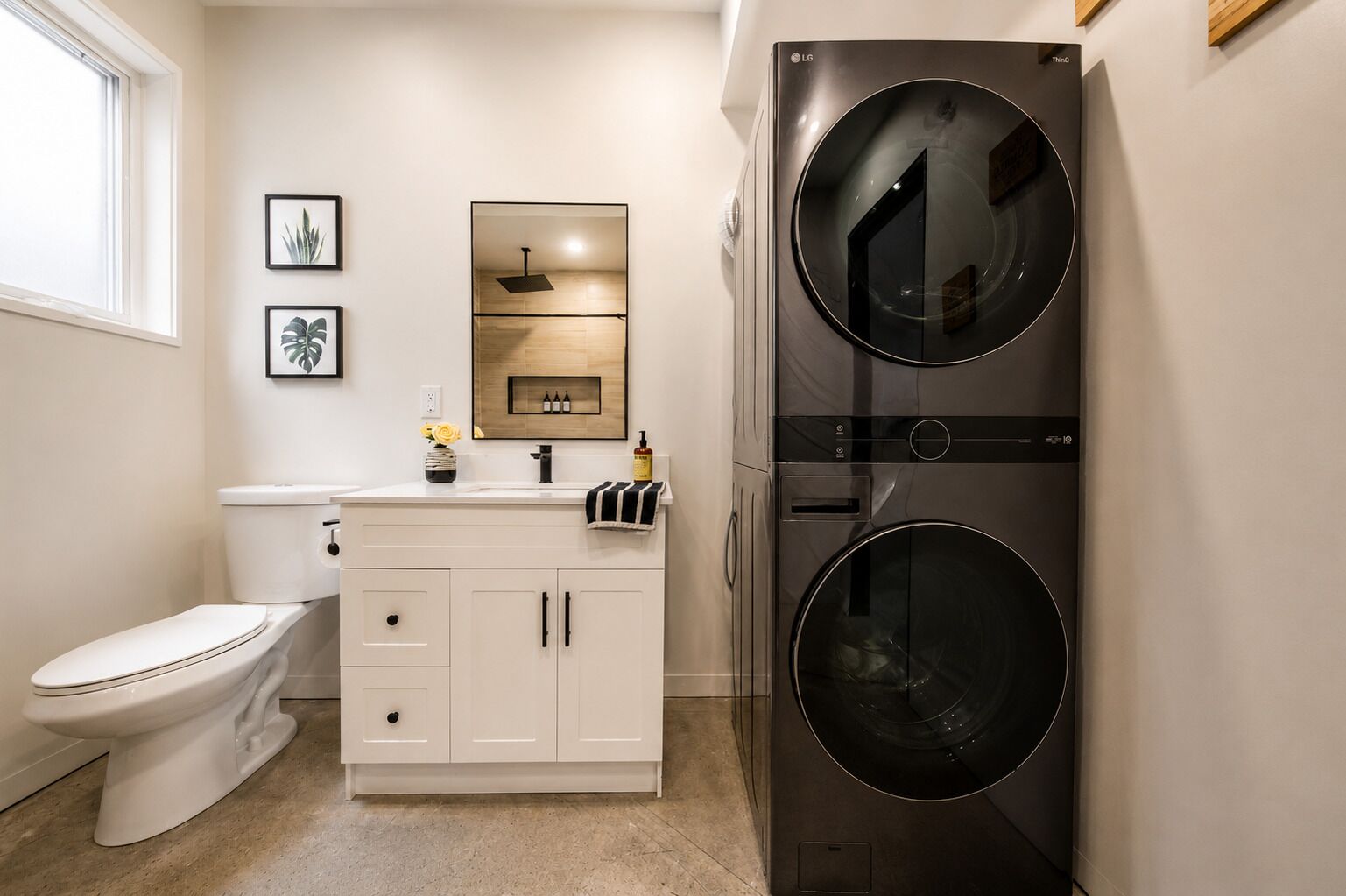 A modern bathroom with a toilet, sink, cabinet, and a stacked washer and dryer unit.