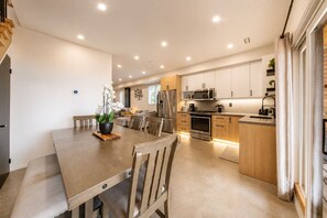 Cocina moderna con armarios de madera, electrodomésticos de acero inoxidable y un comedor con mesa y sillas de madera.