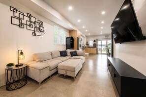 A modern living room with a sectional sofa, a flat-screen TV mounted on the wall, and a small side table with a lamp.