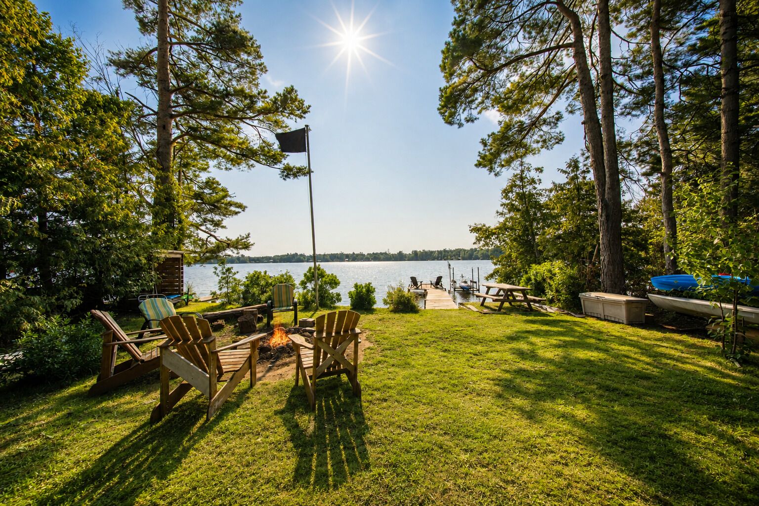 A lakeside outdoor seating area with chairs, a fire pit, and a picnic table.