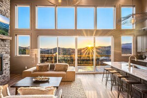 A spacious living area with a large window overlooking a scenic mountain view, a cozy seating area, and a modern kitchen with a large island. - Gorgeous Lux Pool cabin Incredible Views (Sevierville)