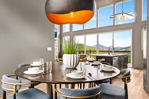 A dining area with a round table set for four, large windows offering a view of the outdoors, and a hanging light fixture above. - Gorgeous Lux Pool cabin Incredible Views (Sevierville)