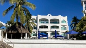 A beachfront hotel with a white facade, multiple balconies, and palm trees. - Breathtaking ocean front condominium in the gated community of Club Santiago (Manzanillo)