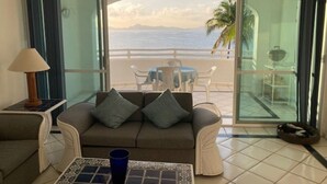 A living room with a sofa, a coffee table, and a view of the ocean through large glass doors. - Breathtaking ocean front condominium in the gated community of Club Santiago (Manzanillo)