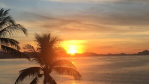 A sunset over a beach with palm trees and beach umbrellas. - Breathtaking ocean front condominium in the gated community of Club Santiago (Manzanillo)