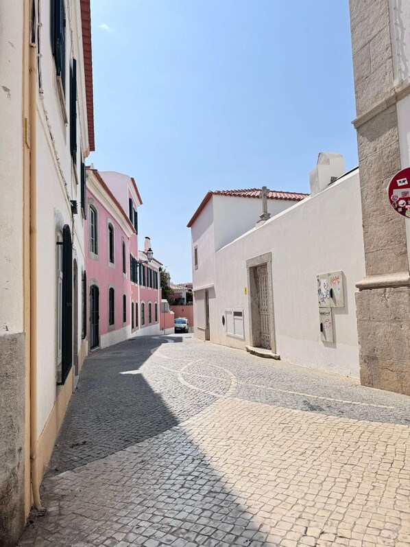 A narrow cobblestone street flanked by buildings with pastel-colored facades and traditional architecture. - The Pearl - Cascais Guest House - City & Beach (Cascais)