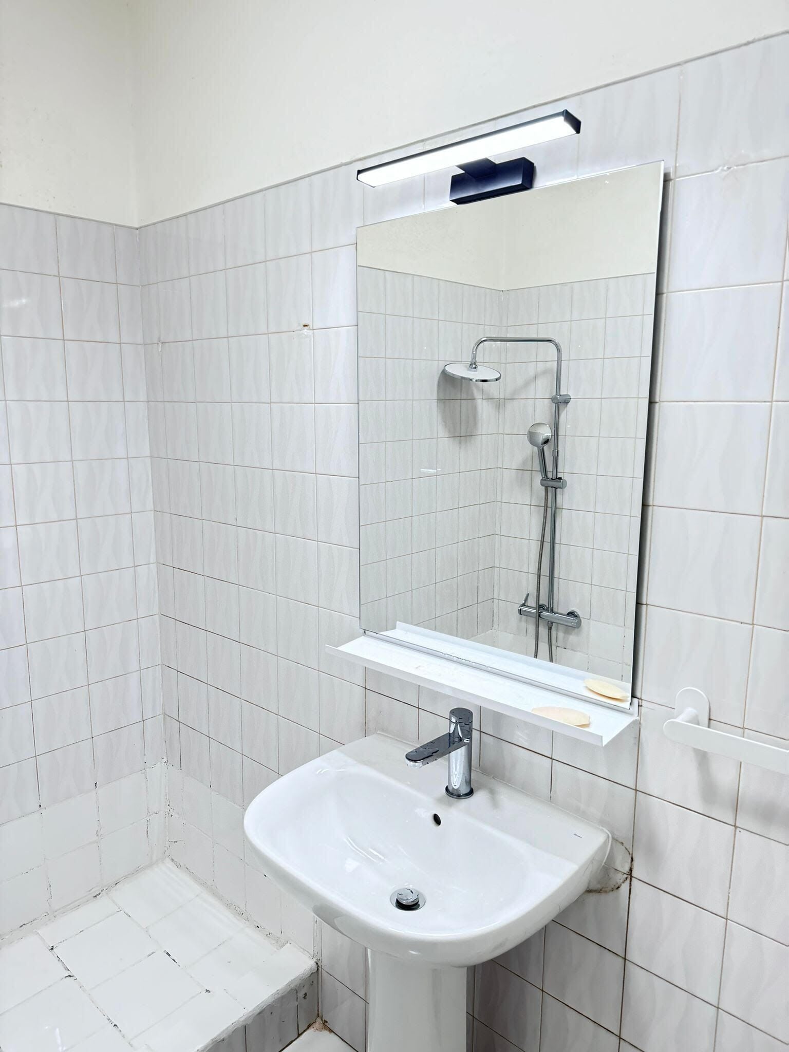 Un baño con azulejos blancos, un lavabo, un espejo y una ducha.