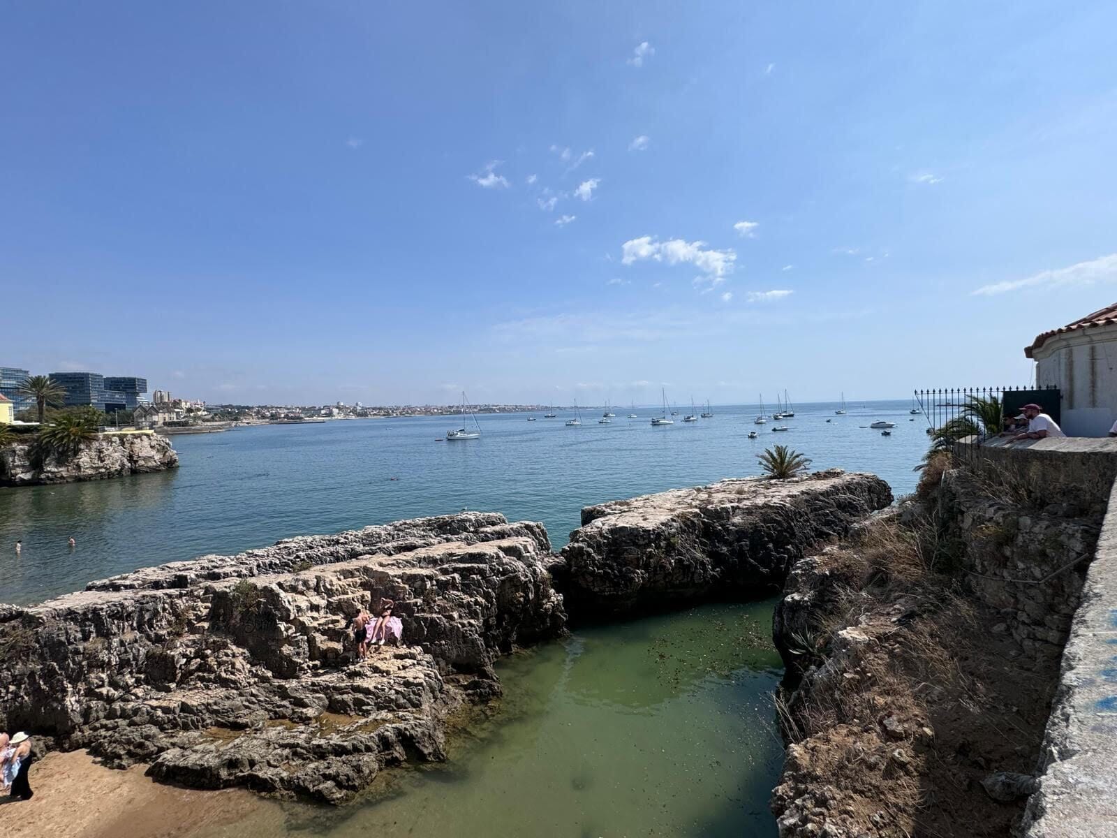 A coastal view with rocky formations, a clear sky, and boats in the water.
