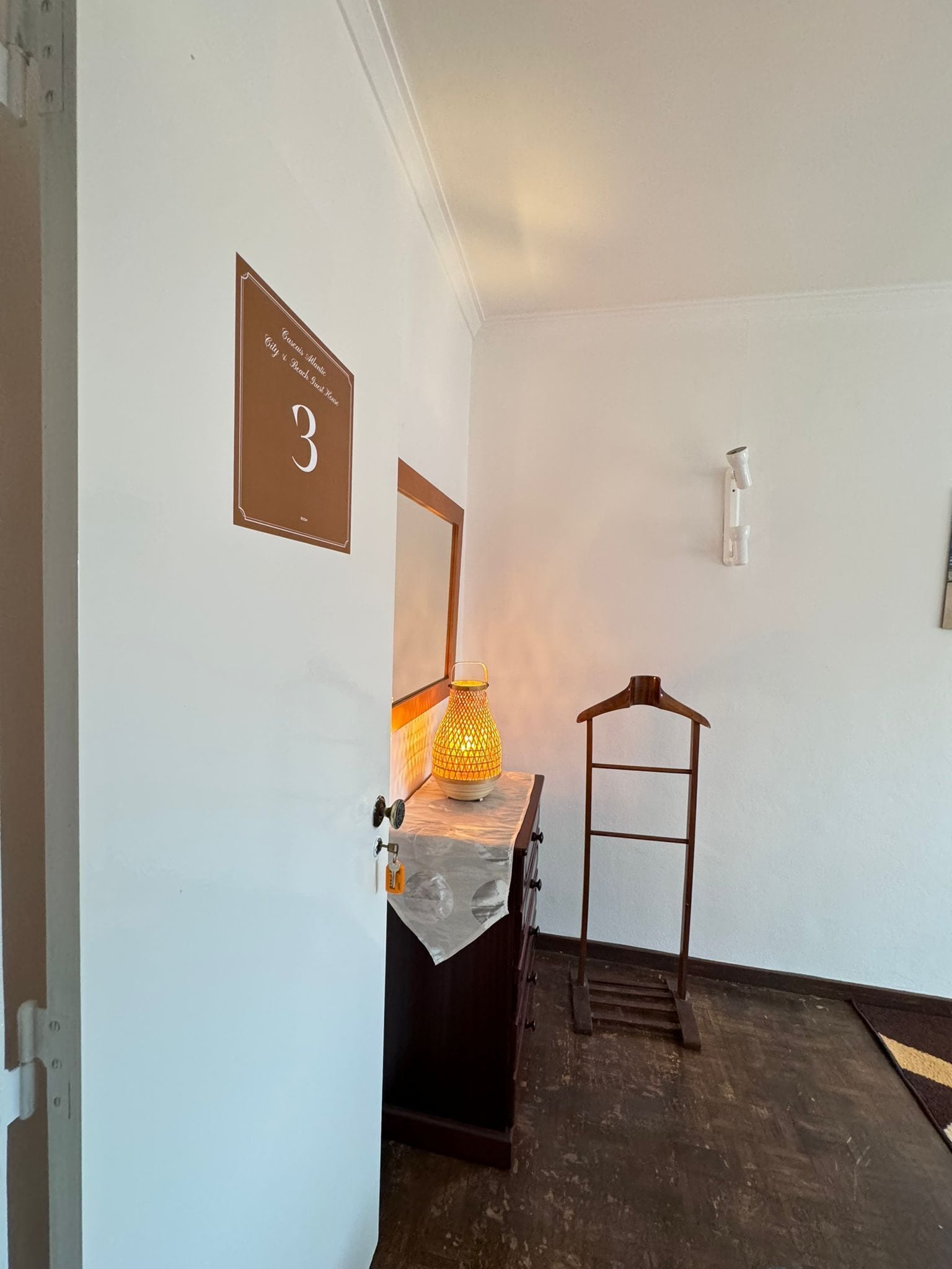 A room with a wooden cabinet, a metal rack, a wall-mounted light fixture, and a door with a number sign.