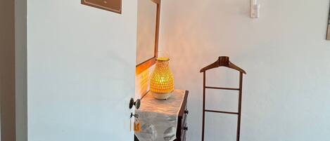 A room with a wooden cabinet, a metal rack, a wall-mounted light fixture, and a door with a number sign.