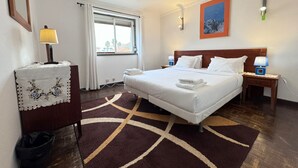 A hotel room with a large bed, a bedside table with a lamp, a window with curtains, a wall-mounted painting, and a patterned rug. - The Pearl - Cascais Guest House - City & Beach (Cascais)