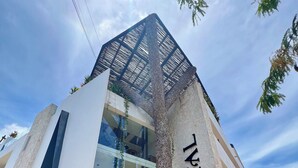 Um hotel moderno com um logotipo 'S' bem visível, amplas janelas de vidro e um design arquitetônico singular com uma parede texturizada e um telhado em treliça.