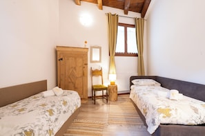 A room with two single beds, a wooden wardrobe, a small table with a lamp, and a window with curtains. - Perla di Villa – Charming House in Vineyard Estate near the Bernina Express (Villa di Tirano)