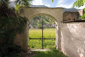 A rustic gate with a metal arch and bars, leading to a grassy area with a mountainous backdrop.