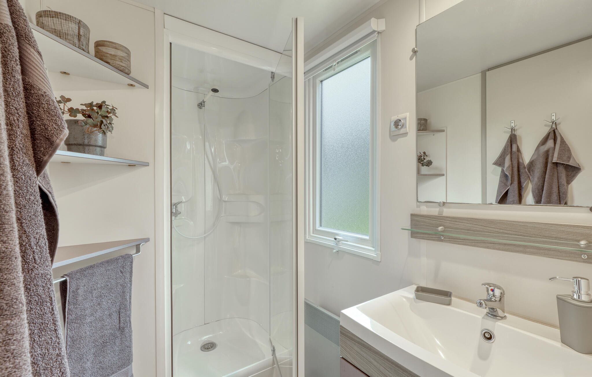 Un bany modern amb dutxa trencada per vidre, un mirall gran i un lavabo blanc.