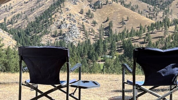 A tent with two black camping chairs facing a mountainous landscape.