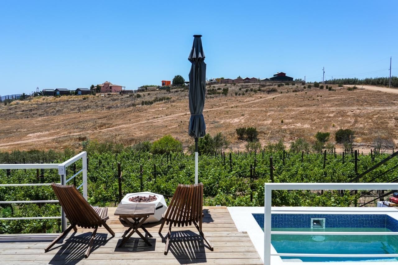 A pool area with a view of vineyards, a wooden deck, and a metal railing.