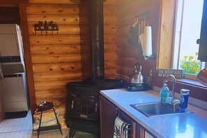 A kitchen with a wood-burning stove, a sink, and a window with a view of the mountains.
