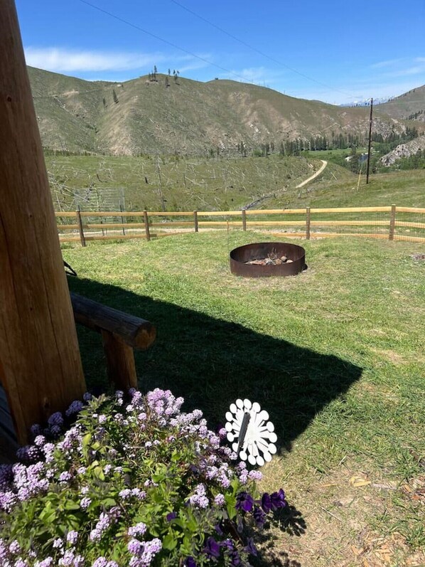 A grassy outdoor area with a wooden fence, a fire pit, and a bench.