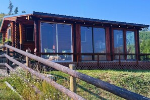 Een houten chalet met grote ramen, een houten terras en een omheining.