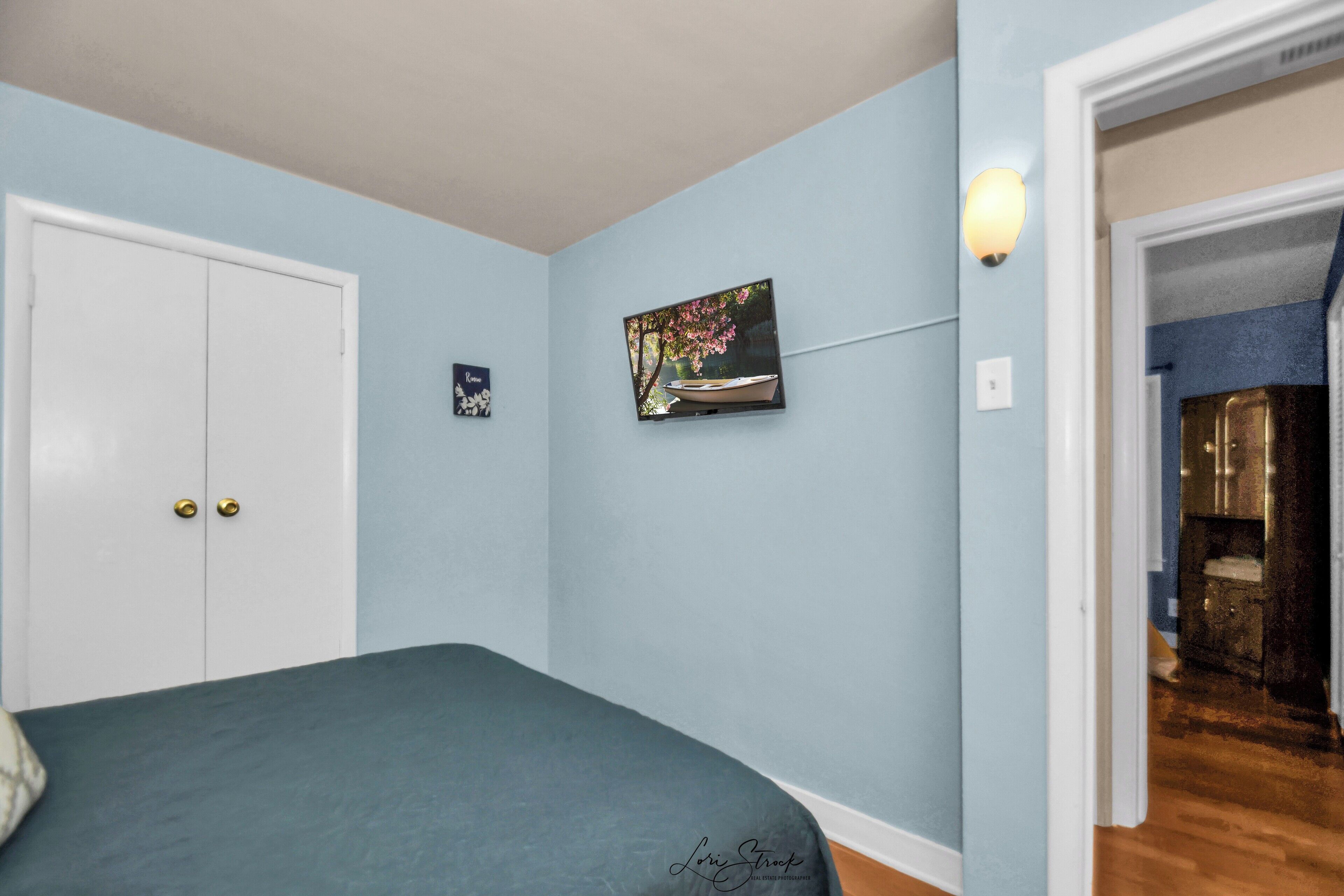 A bedroom with a bed, a white wardrobe, a framed picture, and a wall-mounted light fixture.