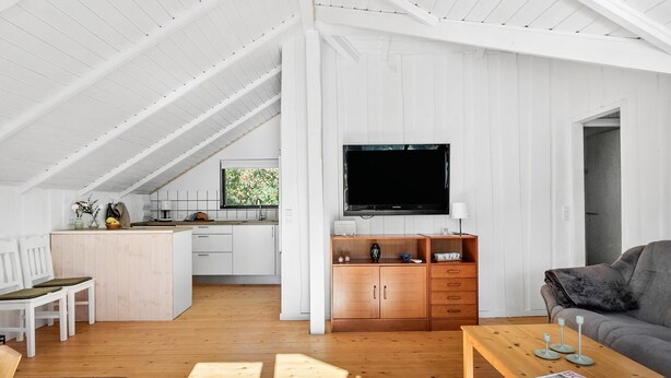 A spacious living area with a wooden floor, a television mounted on the wall, and a cozy seating arrangement.
