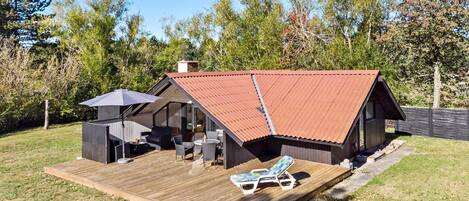 Situated in a wooded area, this cabin features a spacious deck with a seating area and lounge chairs.