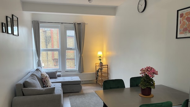 A modern living room with a sofa, a dining table with chairs, a lamp, and a clock on the wall. - Seven Sisters Hideaway (London)