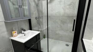 A modern bathroom with a glass-enclosed shower, a sink, and a mirror above it. - Seven Sisters Hideaway (London)