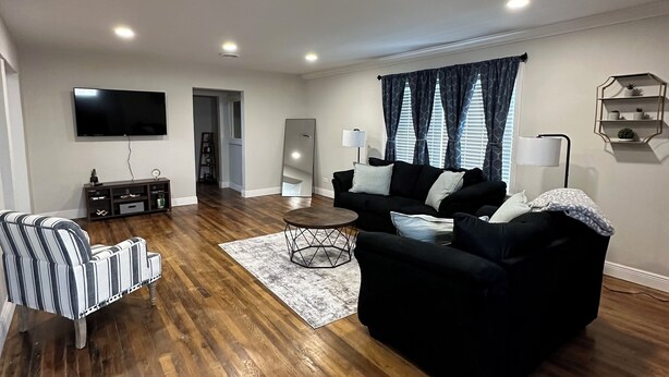 Un salon moderne avec un plancher en bois, un canapé noir, un fauteuil à rayures et un téléviseur à écran plat fixé au mur.