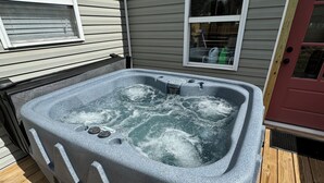 Un bain à remous sur une terrasse en bois, avec une maison en arrière-plan.