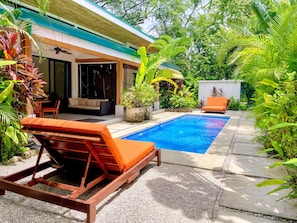 A pool area with lounge chairs, a seating area, and lush greenery.
