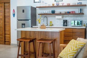A modern kitchen with a central island, wooden stools, and a coffee machine.