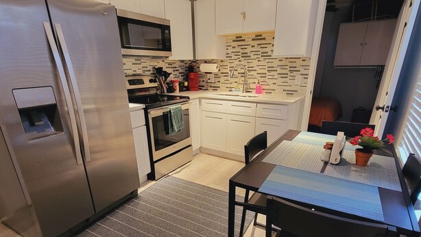 A modern kitchen with stainless steel appliances, a dining area with a table and chairs, and a patterned rug. - Cozy apartment in charming Denton walkable to TWU (Denton)