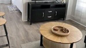 A modern living room with a dark wooden cabinet, a round wooden coffee table, and a television on a stand. - The Suites at The George 212 (Klamath Falls)