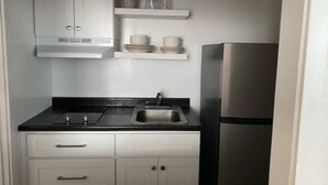 Una cuina compacta amb armaris blancs, un taulell negre, un frigorífic d'acer inoxidable i un rentaplat.