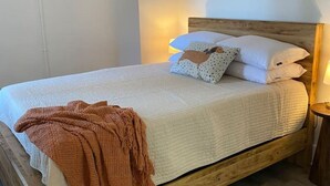 A bedroom with a wooden bed frame, white bedding, and a brown throw blanket. - The George 316 an Art Deco Escape (Klamath Falls)