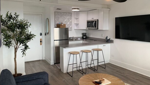 Une cuisine moderne dotée d’un îlot central, de tabourets de bar, d’un ventilateur de plafond et d’un grand téléviseur à écran plat.