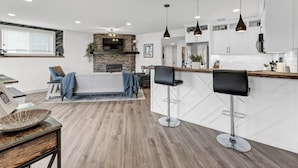 A modern kitchen with a central island, bar stools, pendant lighting, and a stone fireplace.