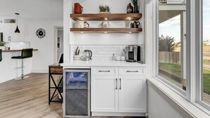 A modern kitchen with white cabinets, wooden shelves, and a built-in dishwasher.