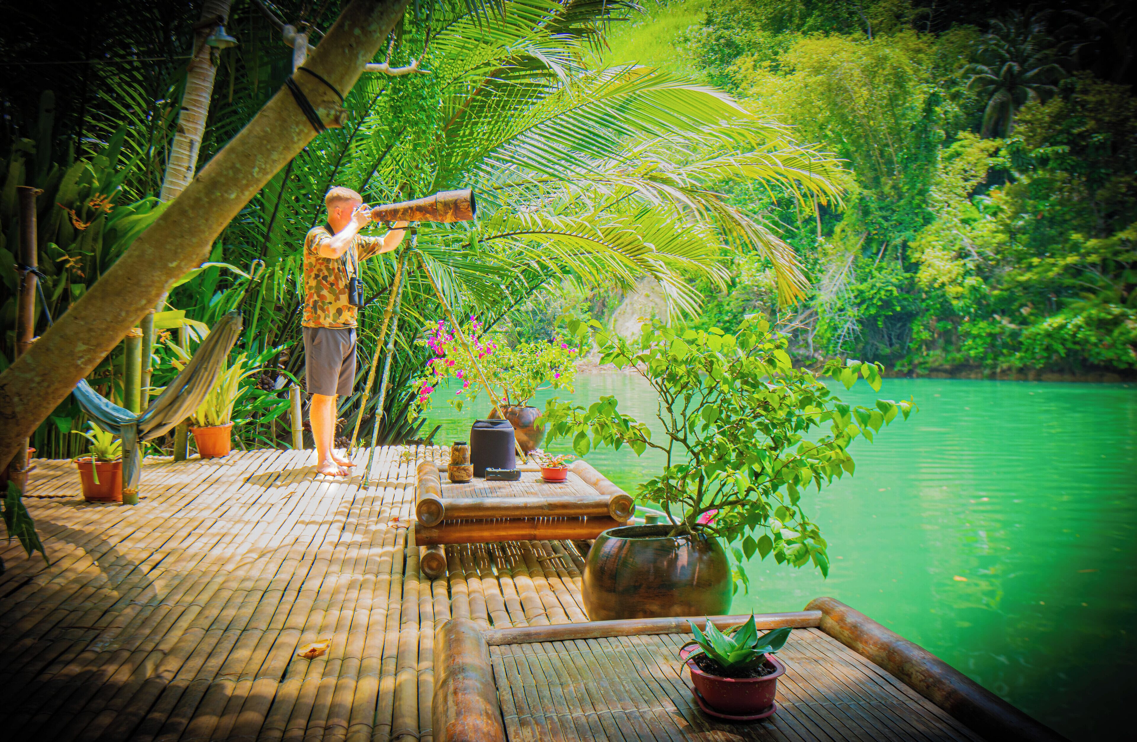 A bamboo deck with a view of a green lake, surrounded by lush tropical vegetation.