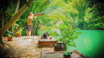 A bamboo deck with a view of a green lake, surrounded by lush tropical vegetation.