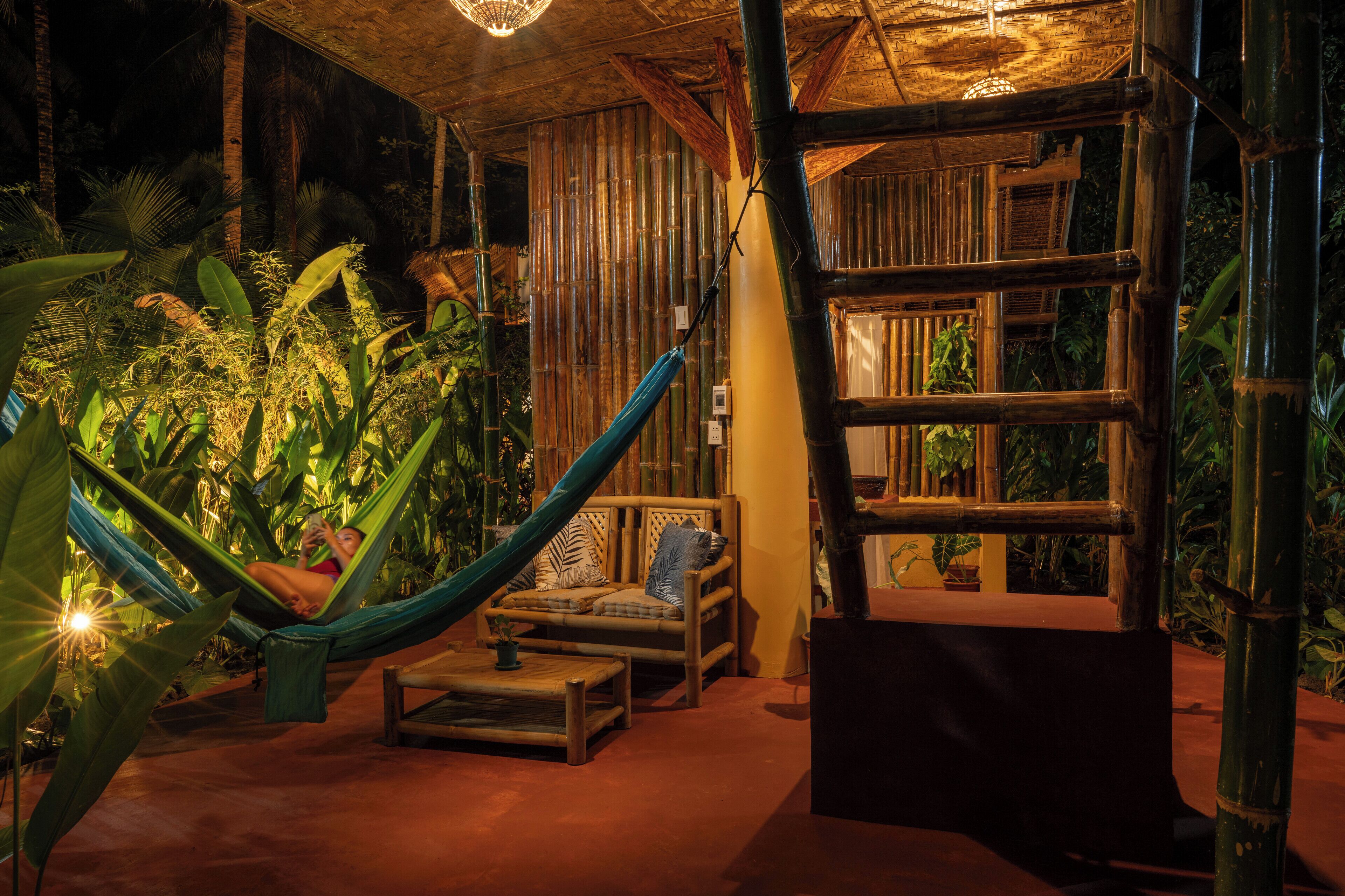 Una silla hamaca, un banco de madera y una mesita con una planta en maceta, todo en un entorno tropical.