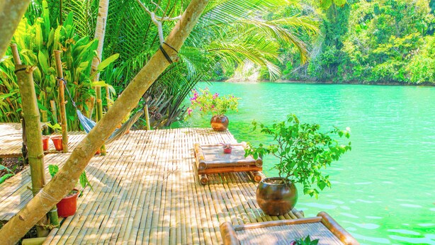 A bamboo deck with seating and potted plants overlooking a body of water. - Water To Forest Ecolodge (Loboc)