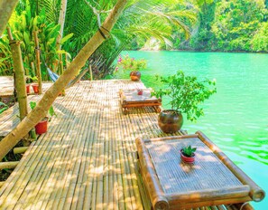 A bamboo deck with seating and potted plants overlooking a body of water. - Water To Forest Ecolodge (Loboc)