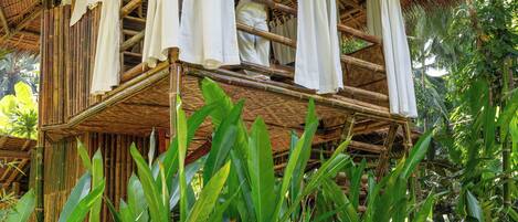 A bamboo structure with a balcony, surrounded by lush greenery.