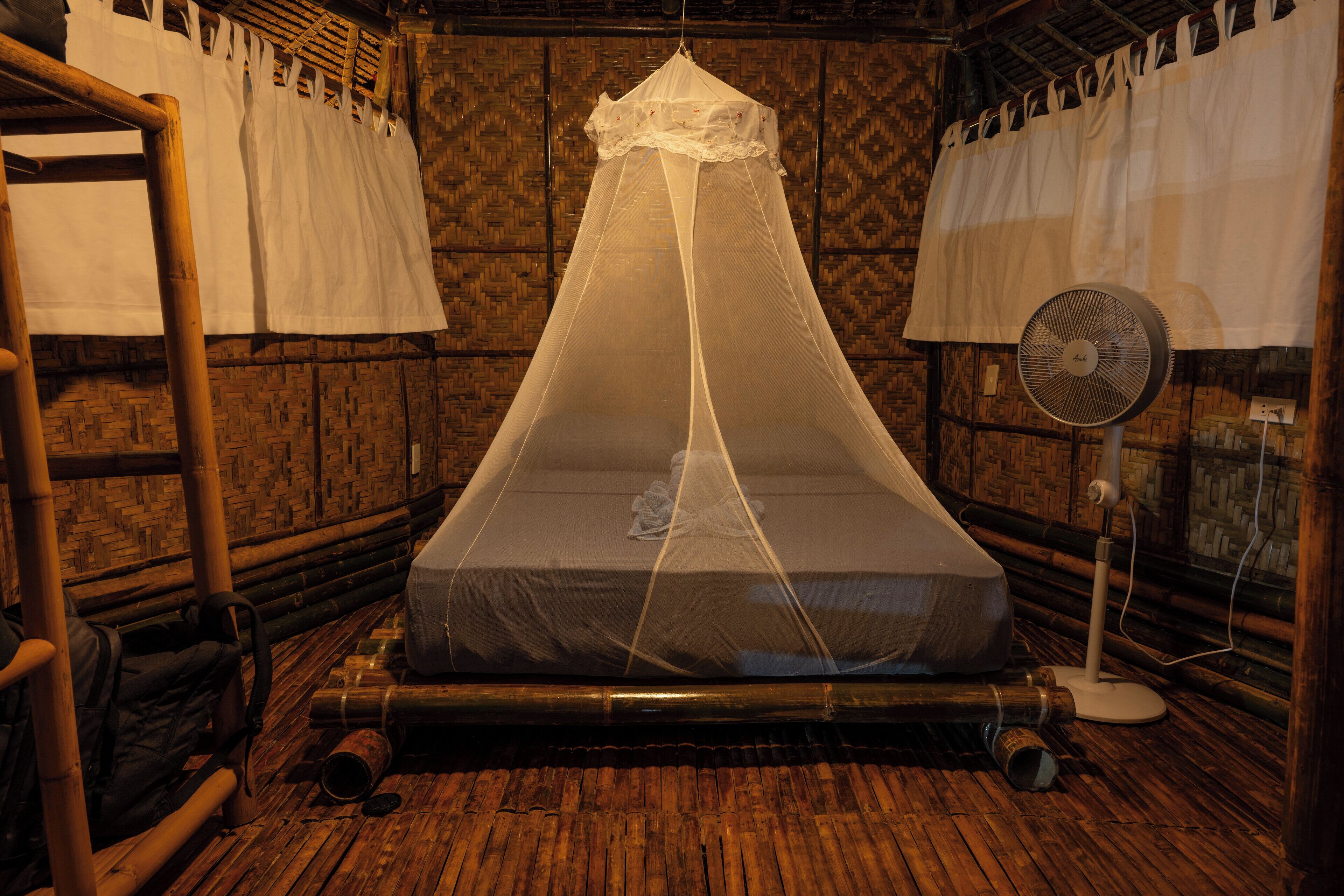 Una habitación con mosquitero sobre la cama, un ventilador y paredes de madera.